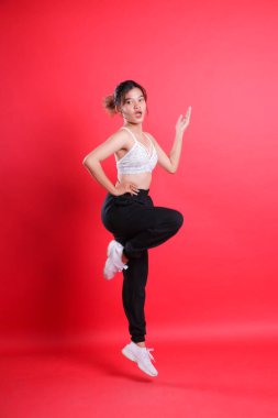 Beyaz spor bluzlu ve siyah pantolonlu bir kadın havada, kırmızı arka planda izole edilmiş kırmızı bir zemine atlıyor gibi görünüyor.