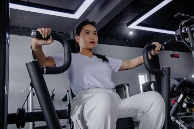 Kararlı genç bir kadın spor salonunda sağlıklı ve aktif bir yaşam tarzını benimseyerek vücudunun üst kısımlarını güçlendirmek için bir kelebek makinesi kullanıyor..