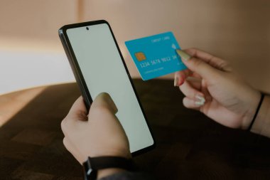 Ticarette dijital ve modern yaşam tarzlarını temsil eden, kapalı bir yerde kredi kartıyla işlem yapmak için akıllı telefonunu kullanan bir kişinin yakalanması.
