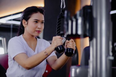 Spor salonundaki triseps egzersizleri için ip çekme ekipmanı kullanan çekici, genç bir esmer kadın spor yaparken azim ve odaklanma gösteriyor..