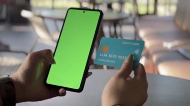 Bireyin elinde yeşil ekranlı bir cep telefonu ve ulaşılamaz bir kredi kartı var. Cep telefonu ödemeleri ve çevrimiçi işlemleri gösteriyor. Finansal iş temaları için ideal.