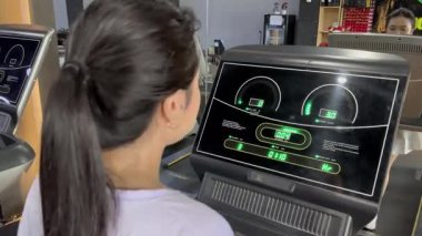 Daha sağlıklı bir vücut yapmak için spor salonunda koşu bandı kullanan genç bir kadının yakın plan fotoğrafı. Odaklanmış ve kararlı. Bu modern spor salonu çeşitli ekipman seçenekleri sunuyor.