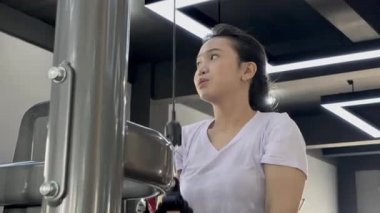 Modern bir spor salonunda, kararlı bir Asyalı kadının kablo kullanırken yakın plan fotoğrafı. Güç eğitimine ve aktif refaha odaklanmış, güçlü bir yaşam tarzı yaratmaya..