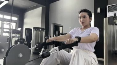 Kablo sırası egzersizine odaklanmış genç bir kadın modern bir fitness merkezinde güç ve dayanıklılığı artırıyor. Bu resim sağlıklı bir yaşam tarzına bağlılığını gösteriyor..