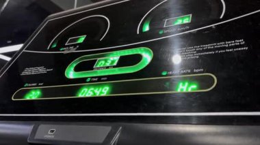 Modern bir koşu bandının konsoluna yakın plan, hız, mesafe, zaman ve kalp hızı gibi ölçümleri parlak yeşil dijital aydınlatmayla gösteriyor. Çalışma verileri gösteriliyor.