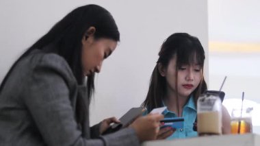 İki arkadaş kafede kahve içerken dijital finans işiyle ilgileniyorlar, kredi kartları ve akıllı telefonlar kullanıyorlar. Modern ticaret ve bankacılık yaşam tarzının bir fotoğrafı..