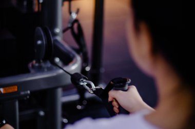 Odaklanmış bir kadın spor salonunda halat çekme makinesi kullanırken egzersiz rutini yapıyor. Güç ve zindelik için kol ve kol kaslarını çalıştırıyor ve çalıştırıyor..