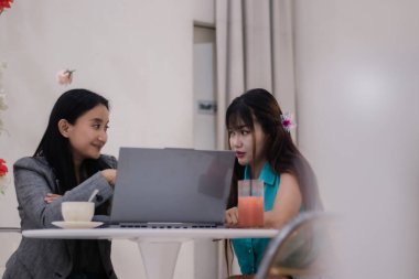 Bir kafede proje üzerinde işbirliği yapan, verileri inceleyen ve fikirlerini dizüstü bilgisayarda paylaşan iki odaklı genç kadın, içki de dahil. Takım çalışması ve iş tartışması.