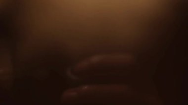 Sıcak ışıkla aydınlatılmış, deride parlayan su damlacıklarını gösteren, duştaki bir kişinin soyut videosu.,