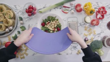 KYIV, UKRAINE - 27 Eylül 2021: Kadın mutfakta sebzeli ve peynirli sağlıklı salata hazırlıyor. Ev hanımı salata için doğranmış peyniri kaseye koyar.