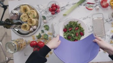 KYIV, UKRAINE - 27 Eylül 2021: Kadın doğranmış sebzeleri kaseye koyar ve sıcacık mutfakta sağlıklı salata yapar. Ev hanımı ev yapımı sebzeli salata hazırlıyor.