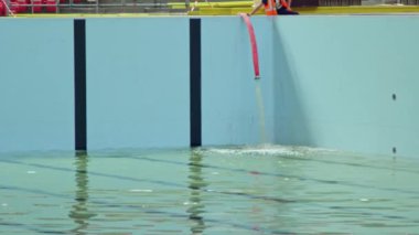 İnşaat alanındaki işçi kontrolü altındaki büyük yüzme havuzuna filtrelenmiş su dökülüyor. Çağdaş spor etkinlikleri için alan