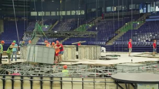 労働者は観客の場所に対してスイミングプールフレーム上の大きなブロックを運ぶ制御します スポーツ複合施設建設現場 — ストック動画