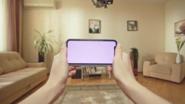 Kahverengi saçlı kadın akıllı telefondan ilginç ve heyecanlı videolar izliyor. Neşeli bayan kendi evinde video izlemekten hoşlanıyor.