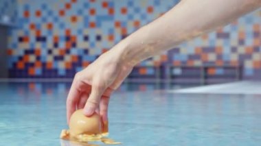 Kadının eli küçük bebeği temiz mavi suya daldırıyor. Yüzme havuzunda profesyonel su altı oyuncağı vuruşu