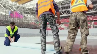 KYIV, UKRAINE - 27 Eylül 2021: İşçiler yüzme havuzu için zemin kaplamak ve süpürge ile temizlemek için özel kaplama kullanır. Deneyimli adamlar spor turnuvaları için yeni bir alan inşa ediyorlar.
