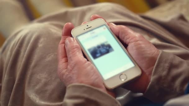 シニア女性は 現代のスマートフォンを介して友人とチャットで写真がロードされるのを待ちます 革新的なガジェットの閉鎖を保持年金受給者のしわの手 — ストック動画