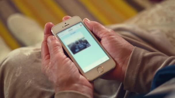 年配の女性は友人とチャットで画像がロードされるのを待ちます 背景がぼやけている上にスマートフォンを保持年金受給者の手をしわ — ストック動画
