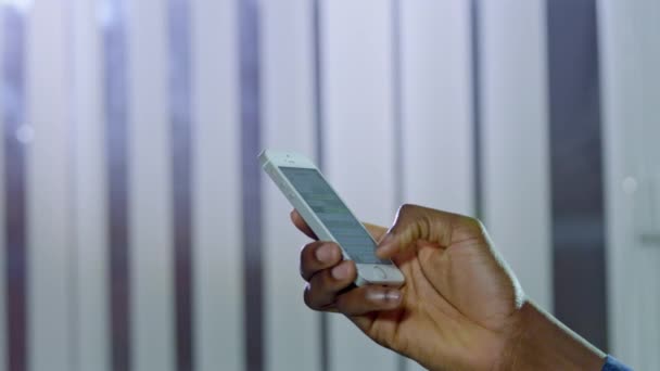 アフリカ系アメリカ人のユーザーの手は ウィンドウ上のブラインドに対してモダンなスマートフォンを保持 人は電子機器の近くでソーシャルネットワークをチェックする — ストック動画