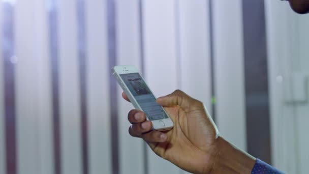 アフリカ系アメリカ人の男性は 現代のスマートフォンにメッセージを入力します 白いブラインドに対してガジェットを保持する人の手は 光の風の接近に手を振る — ストック動画