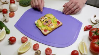 Kadın sebze ve peynir parçalarıyla sağlıklı atıştırmalıklar sergiliyor. Ev hanımı menekşe kesim tahtasında sandviç hazırlıyor.
