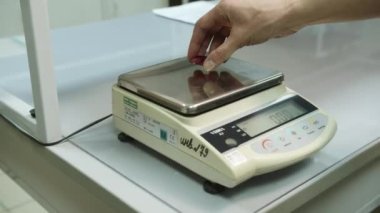 KYIV, UKRAINE - 27 Eylül 2021: Laboratuvar asistanı bitmiş ürünün ağırlığını ölçer. Kırmızı termal çamaşır makinesi elektronik ölçekte. Laboratuvar kalite kontrolü gerçekleştiriyor