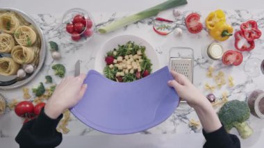 Ev hanımı doğranmış peynir koyar ve taze sebzelerle sağlıklı salata yapar. Kadın plastik kesme tahtası kullanarak yemek hazırlıyor.