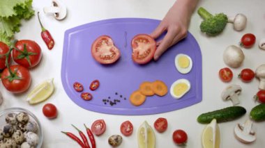 Kadın domatesi menekşe dilimleme tahtasıyla ikiye böler ve sağlıklı salata için malzemeler hazırlar. Ev hanımı mutfakta sebze doğruyor.