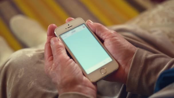 老年妇女躺在沙发上聊天时收到照片信息 在模糊的背景特写下 现代智能手机和退休人员皱巴巴的双手 — 图库视频影像