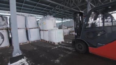 İşçiler kış günü inşaat malzemeleri paketlerini elektrikli forkliftle kaldırır ve taşır. Modern polikarbonat panelleri ve film bobinleriyle dolu bir depo.