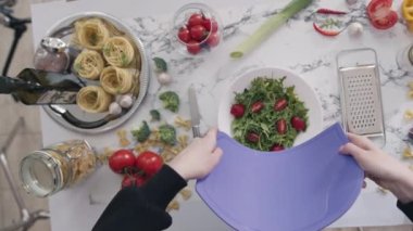 KYIV, UKRAINE - 27 Eylül 2021: Kadın doğranmış sebzeleri kaseye koyar ve sıcacık mutfakta sağlıklı salata yapar. Ev hanımı ev yapımı sebzeli salata hazırlıyor.