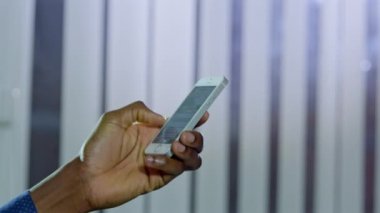 Pencerelerde panjurlara karşı modern aletler tutan Afro-Amerikan bir adamın eli. Erkek kullanıcı, arkadaşa yakın çekim yapmak için akıllı telefondan mesaj yazar