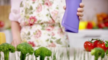 Ev hanımı, rahat mutfağa karşı esnek bir kesim tahtası gösteriyor. Önlük takan kadın, brokoliye karşı menekşe kesim tahtasının esnekliğini gösteriyor