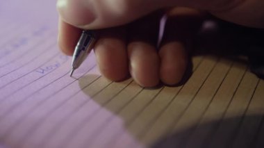 Elinde kalem tutarak sorulan soruların cevaplarını kağıda yazan bir adam. Erkek kişi, günlükte kişisel duygularını yakın planda paylaşır.