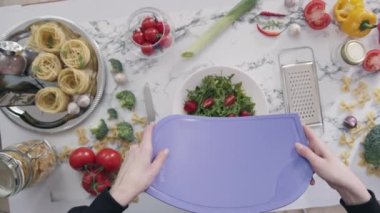 Ev hanımı mutfakta taze sebzelerle sağlıklı salata hazırlıyor. Kadın iyilikle ilgilenir ve doğranmış sebzeleri kaseye koyar.
