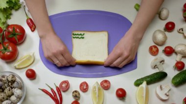 Ev hanımı panoda sebzeli sağlıklı sanviç hazırlıyor. Kadın taze ekmeğin üzerine peynir koyar ve güzel sandviç yapar.