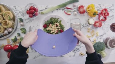 Ev hanımı, plastik kesme tahtasındaki peyniri evde sebze salatasıyla birlikte kaseye koyar. Ev yapımı salata yapan kadın sağlığa önem verir.