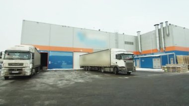 KYIV, UKRAINE - 27 Eylül 2021: Kamyonlar modern yapı malzemeleri deposunun kapılarının yanında duruyor. Ahşap paletler, bulutlu gökyüzünün altında endüstriyel üretimin yanında kar tozuyla kaplı asfalt üzerinde duruyor.