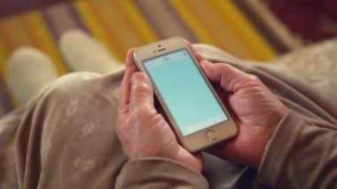Kanepede oturan büyükannenin buruşuk ellerinde modern akıllı telefon. Yaşlı kadın internet sohbetlerinde iletişim için aygıt kullanıyor.