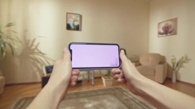 ALMATY, KAZAKHSTAN - 14 Eylül 2020: Kahverengi saçlı kadın hafta sonunu telefonuyla kendi dairesinde geçirmekten hoşlanıyor. Gülümseyen bayan dokunmatik ekranı tutuyor ve keşfediyor ve kanepeye oturuyor.