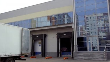 Kamyon, cam duvarları ve pencereleri olan bir depoya mal götürüyor. Hafif kamyon sürücüsü malları boşaltmak için depo kapısının önüne park ediyor.