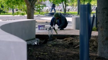 Şehir işçisi, şehir parkındaki fıskiyenin yakınına asfalt döşemiş. Kişi düzeyi kauçuk çekiçle kaldırım döşemeleri doğru bir şekilde