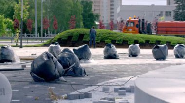 Şehir işçisi şehir parkında çim biçmeden önce kara toprağı kazıyor. Su makinesi yeşillik serpmeye hazır.