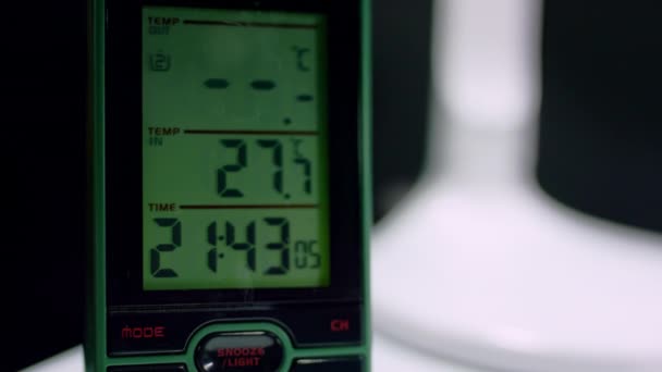 グリーンデジタル時計は暗闇で21 43時間を示しています 電子時計は時間と温度を示す研究室のテーブルの上に立っています — ストック動画