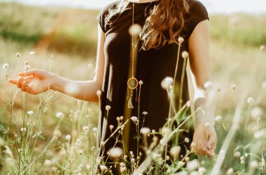 Orta bölüm boho tarzı elbise. Çimenlerde yürüyen genç bir kadın ve doğa ile bağ kuran kır çiçekleri. Kavram: maneviyat, zen, denge, denge, farkındalık