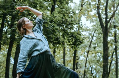 Yoga yapan kadın ormandaki ağaçlarla barışçıl savaşçı pozu veriyor.