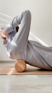 Spor kıyafetli kadın sırt kasları yapıyor. Mantar rulo üzerinde miyofasyal gevşeme.