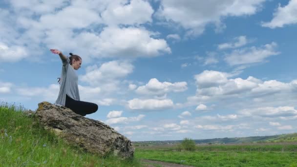 一个女人坐在田野里的岩石上 高高地举着胳膊 — 图库视频影像