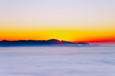 Dağların arkasından doğan altın güneş bulutlardan oluşan denizi aydınlatıyor.