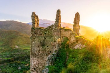 Güzel gün batımı ya da eski kalıntıların gündoğumu bir tepenin tepesinde, arkasında beyaz kar olan yeşil dağlar.